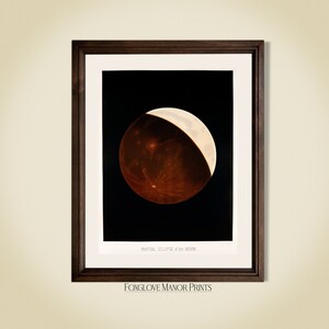 May include: Framed print of a partial lunar eclipse. The image shows a dark brown and white moon against a black background. The print is in a dark brown wooden frame with the text "PARTIAL ECLIPSE of the MOON" and "FOXGLOVE MANOR PRINTS".