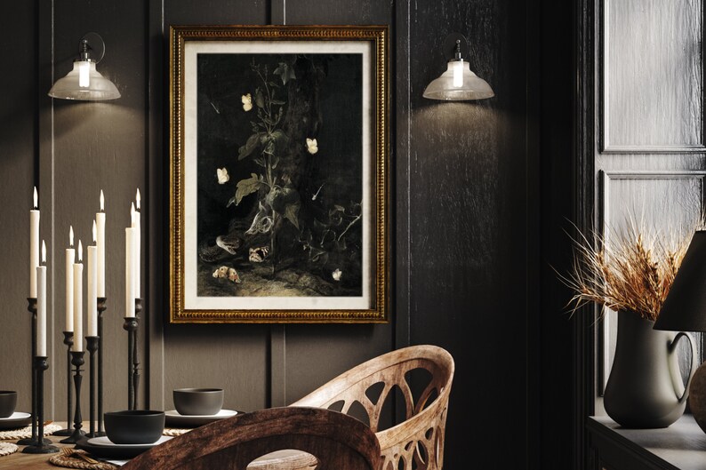 May include: A framed black and white still life print of a plant with white flowers and butterflies. The print is in a gold frame and is hanging on a dark wall. There are candles and a table setting in the foreground.