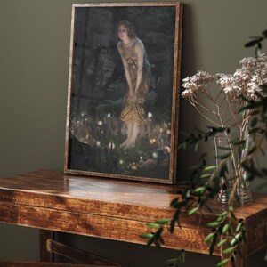 Op de afbeelding: Een ingelijst schilderij van een vrouw in een bosrijke omgeving. De vrouw draagt een lange, vloeiende jurk en een kroon van bloemen. Ze wordt omringd door kleine, gloeiende lichtjes.