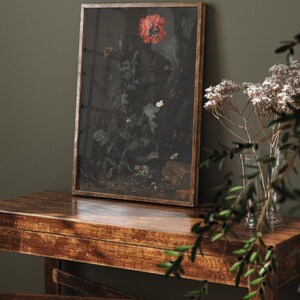 May include: A framed print of a still life featuring a red poppy flower, green leaves, and insects. The print is in a wooden frame and is hanging on a dark green wall.