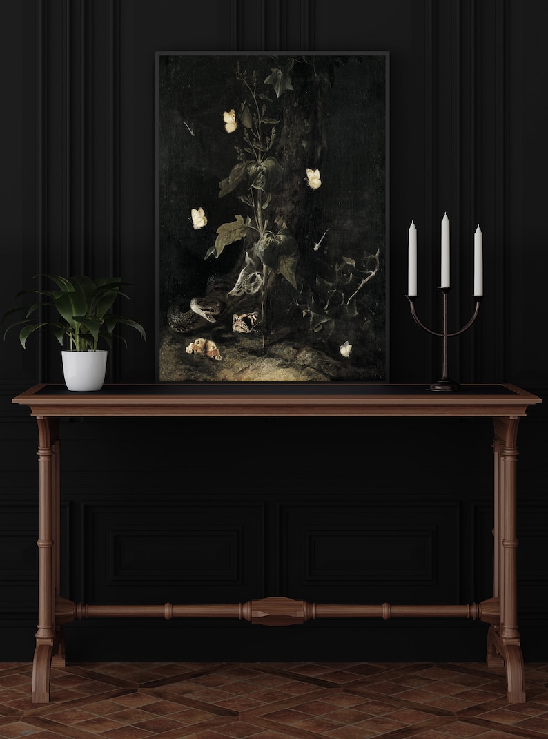 May include: A dark, framed painting of a still life featuring a snake, a skull, and a plant with white butterflies. The painting is hanging on a black wall above a wooden console table with a potted plant.