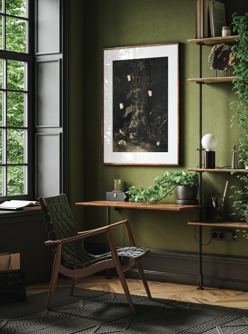May include: A dark wood desk with a black leather chair, a framed botanical print, and a shelf with plants and a lamp. The room has dark green walls and wood floors.