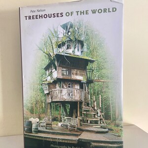 May include: A book titled "Treehouses of the World" by Pete Nelson with a photograph of a large wooden treehouse with a wooden deck and stairs. The treehouse is surrounded by trees and a wooden barrel.