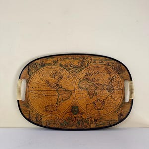 May include: Oval serving tray with a vintage world map design. The tray has a black border, cream-colored handles, and a detailed depiction of the continents and oceans. The map is in shades of brown and beige.