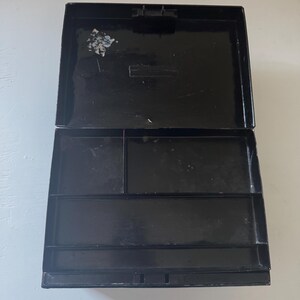 Puede incluir: Caja rectangular negra abierta, con tapa con bisagras. El interior est&aacute; dividido en varios compartimentos de diferentes tama&ntilde;os. La caja parece estar hecha de un material brillante, y la tapa est&aacute; ligeramente entreabierta.
