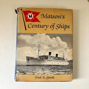 May include: Vintage book titled "Matson's Century of Ships" with a ship illustration on the cover. The cover is tan with black text and a red flag with a white "M" logo. The author's name, Fred A. Stindt, is at the bottom.