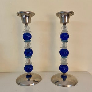 May include: A pair of silver candle holders with blue and white glass beads. The candle holders have a round base and a cup-shaped top.