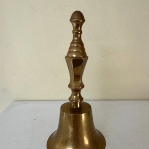 May include: A vintage brass bell with a flared base and a decorative handle. The bell has a warm, golden hue and a classic design, suitable for various decorative purposes. The bell measures approximately 6 inches in height.