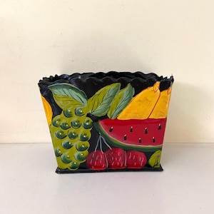 May include: Black metal planter with a scalloped rim, hand-painted with a colorful fruit design. The design features a watermelon, grapes, cherries, and pears.