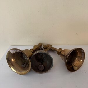 May include: Four antique brass bells with varying handle designs. The bells are arranged on a white surface, showcasing their aged, golden appearance. The bells have a classic, rounded shape, and the handles feature decorative elements.