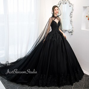 May include: A black tulle ball gown with a lace bodice and a long train. The gown has a sheer cape with a hood.