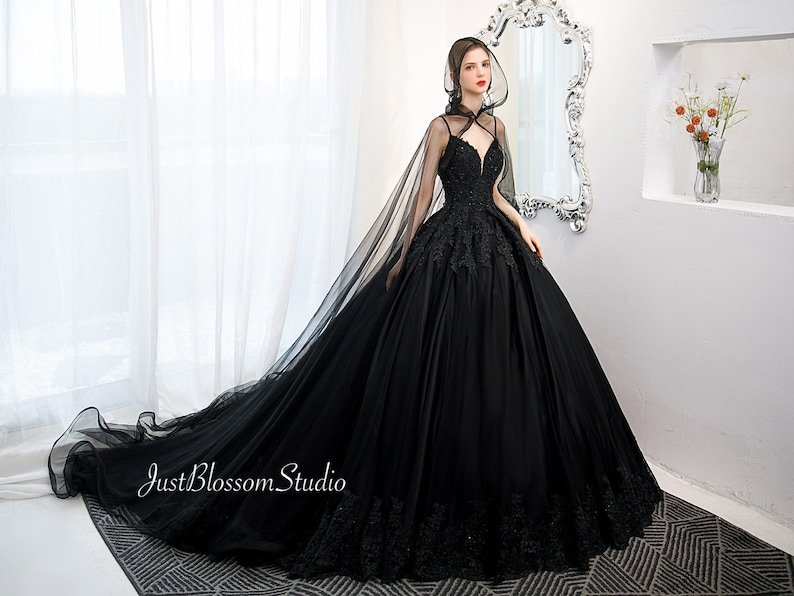 May include: A black tulle ball gown with a lace bodice and a long train. The gown has a sheer cape with a hood.