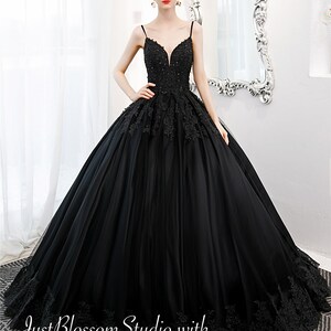 May include: A black tulle ball gown with a sweetheart neckline and lace detailing. The dress has a fitted bodice and a full skirt. The model is wearing the dress with a pair of earrings.