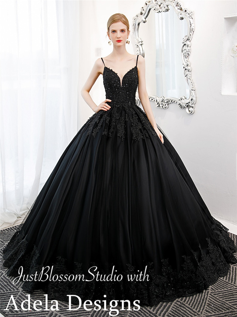 May include: A black tulle ball gown with a sweetheart neckline and lace detailing. The dress has a fitted bodice and a full skirt. The model is wearing the dress with a pair of earrings.