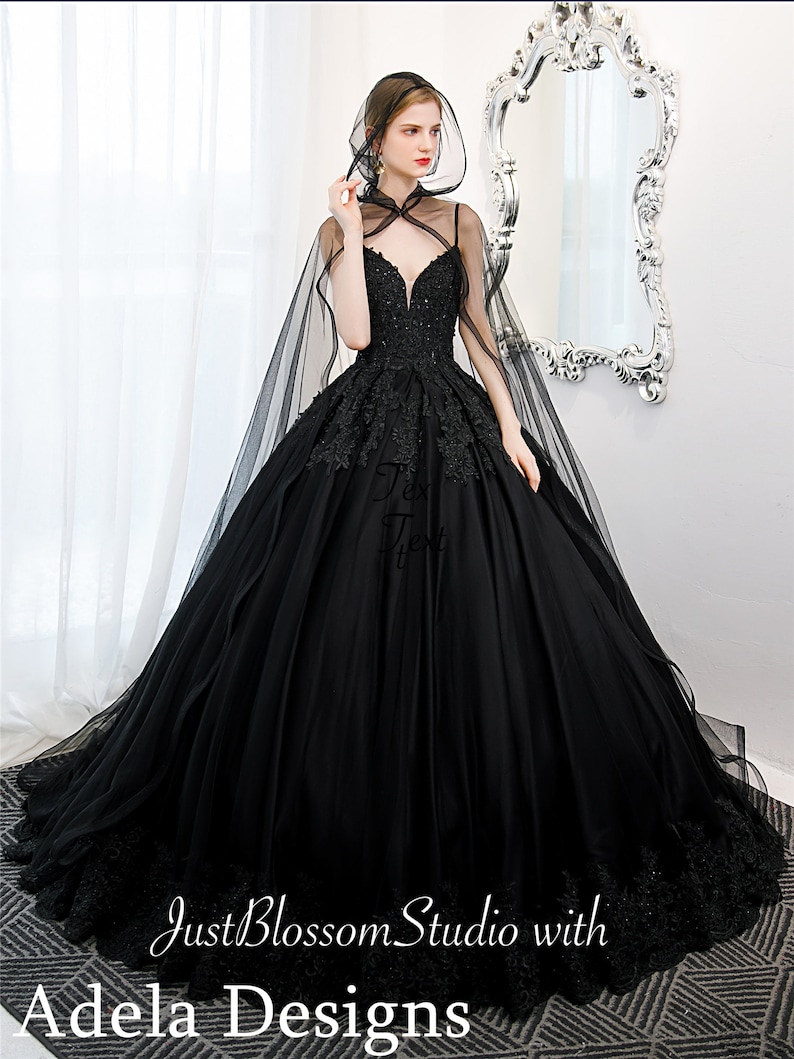 May include: A black tulle ball gown with a lace bodice and a long black tulle cape. The gown has a sweetheart neckline and a fitted bodice. The skirt is full and flowing. The cape has a hood and is trimmed with lace.