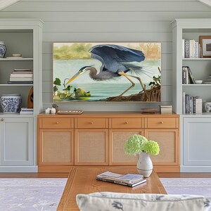 May include: A living room entertainment center with a large framed painting of a blue heron. The center features a light wood cabinet with woven panels, flanked by built-in bookshelves. A coffee table and vase with green flowers complete the scene.