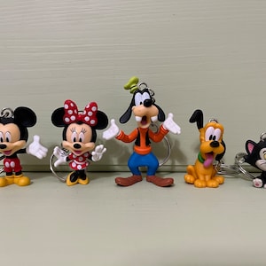 May include: Five character keyrings featuring Mickey Mouse, Minnie Mouse, Goofy, Pluto, and a black and white cat. Each keyring has a silver ring and is made of colourful plastic.