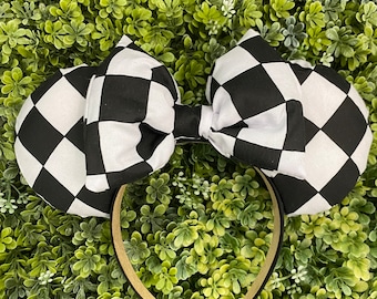 May include: Black and white checkered mouse ears headband with a large bow. The headband is made of a soft, comfortable material and is perfect for any Disney fan.