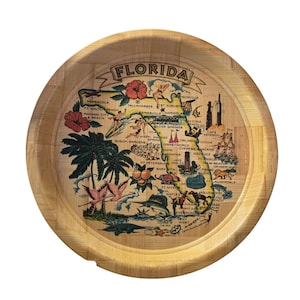 May include: Circular wooden serving tray featuring a map of Florida. The map includes illustrations of palm trees, flamingos, and landmarks. The word "FLORIDA" is at the top in a banner.