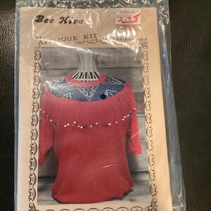 Può includere: Un kit di applique Bee Hive con un maglione rosso con bordi blu e bianchi e perline colorate. Il kit è etichettato "2285 Denim w/ Fringe & Beads".