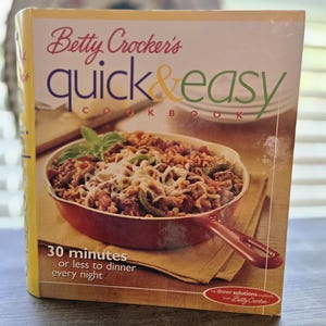 Può includere: La copertina di "Betty Crocker's Quick & Easy Cookbook" mostra un piatto cotto in una padella rossa. Il titolo è in rosso e verde. Il testo recita "30 minuti o meno per la cena ogni sera."