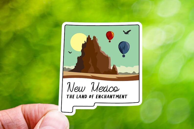 May include: A sticker featuring a stylized illustration of a mountain range with a sun and hot air balloons in the sky. The text "New Mexico The Land of Enchantment" is printed below the image.