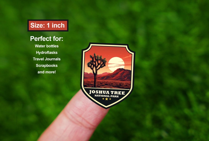 May include: A 1 inch sticker featuring a Joshua Tree National Park design. The sticker has a shield shape with a red, orange, and yellow sunset background. A silhouette of a Joshua Tree is in the center of the sticker. The text "Joshua Tree National Park" is printed in black at the bottom of the sticker.