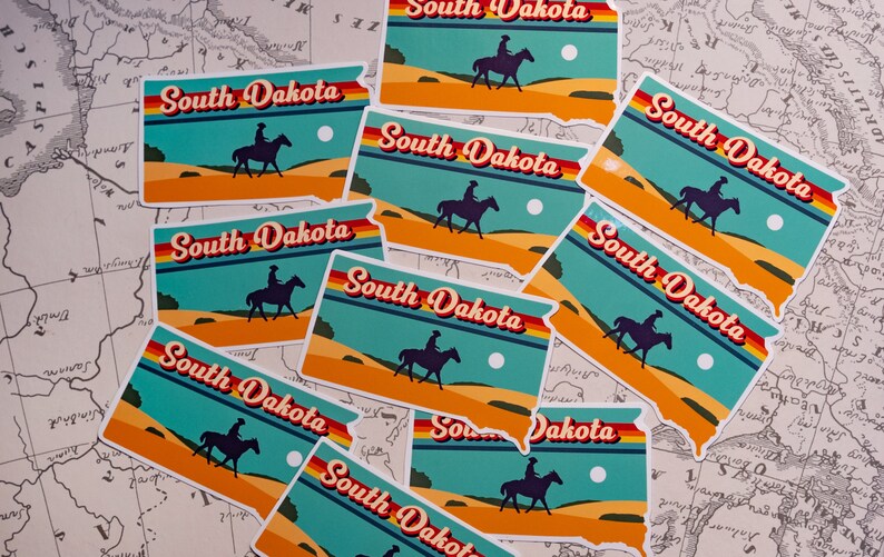 May include: A collection of nine colorful stickers featuring the state outline of South Dakota with the text "South Dakota" in a retro font. Each sticker features a silhouette of a person riding a horse across a desert landscape with a sun and clouds in the background.