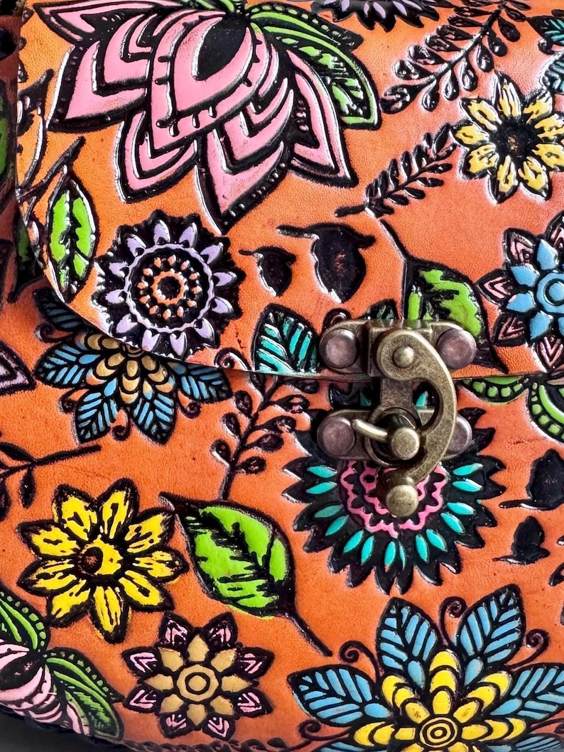 May include: Close-up of a leather bag with a floral design. The bag is orange with embossed flowers in pink, yellow, blue, and green. The bag has a metal clasp.