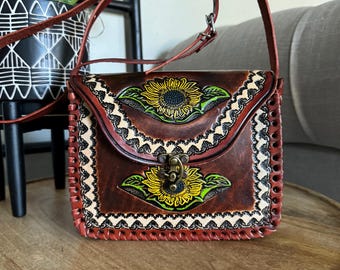 May include: A brown leather crossbody bag with a flap closure and a sunflower design. The bag has a decorative stitched border and a metal clasp.