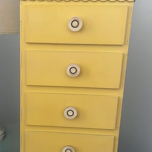 May include: A yellow wooden dresser with four drawers and round wooden knobs. The dresser has a scalloped top edge.