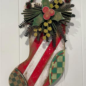 May include: A wooden Christmas stocking with red and white stripes, green and brown checkered fabric, and a green holly leaf and berry embellishment.