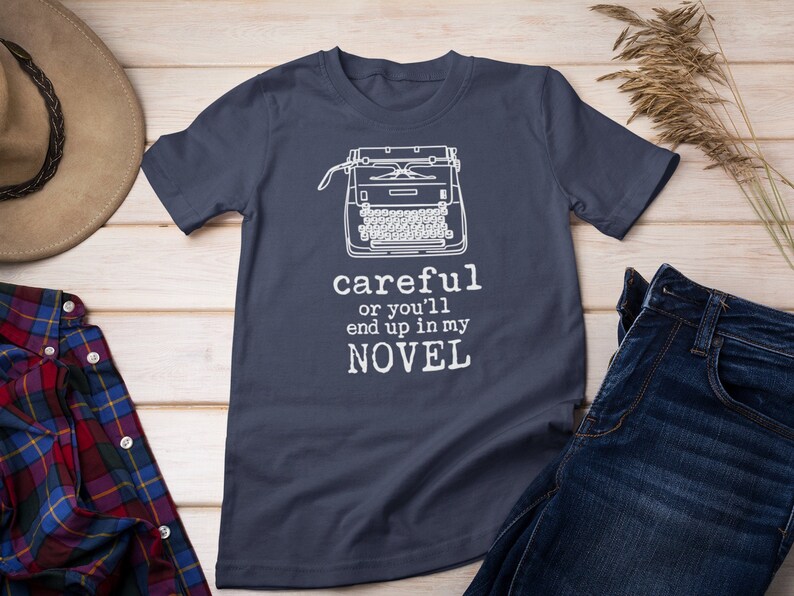 May include: A dark blue t-shirt with a white typewriter graphic and the text "careful or you'll end up in my NOVEL".