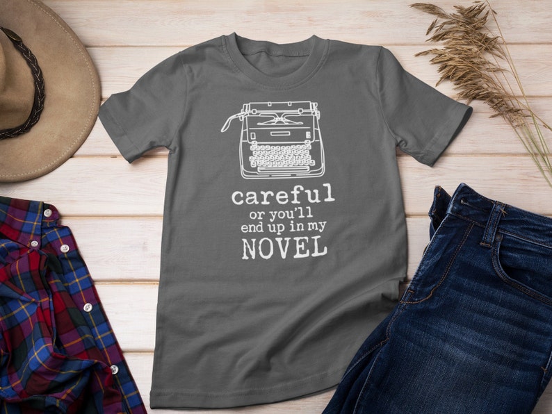 May include: A dark gray t-shirt with a white typewriter graphic and the text "careful or you'll end up in my NOVEL".