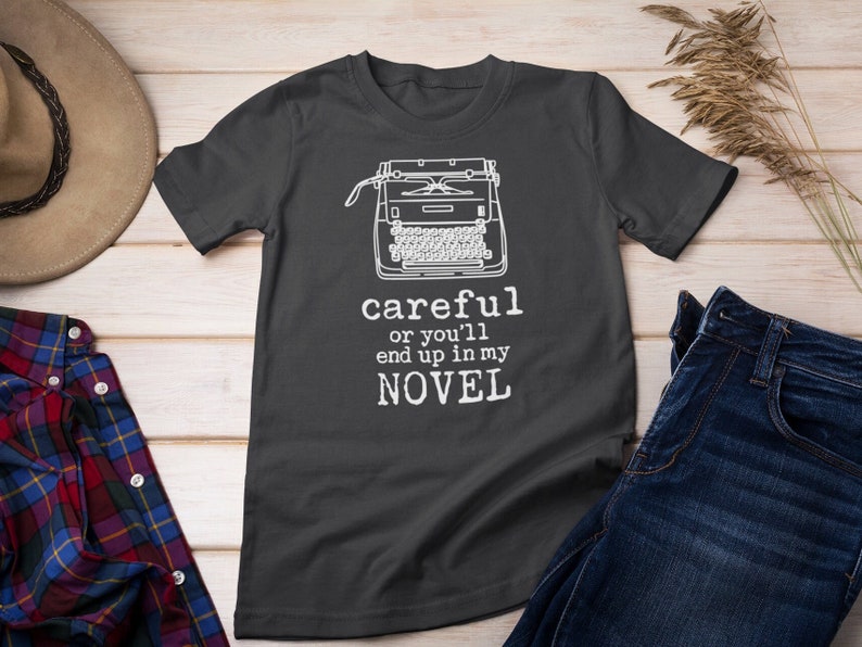 May include: A dark gray t-shirt with a white typewriter graphic and the text "careful or you'll end up in my NOVEL".