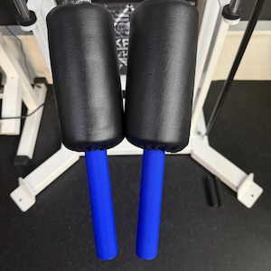 May include: Two gym machine handles featuring black cylindrical padded grips and bright blue textured lower sections. The handles are attached to white vertical support bars, providing a clear view of the grip area and the contrasting color scheme.