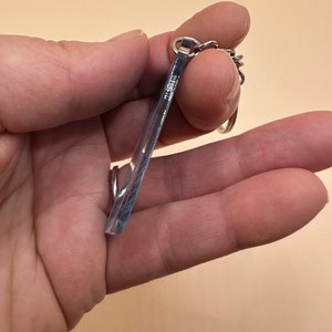 Pode incluir: Um chaveiro de acr&iacute;lico transparente com uma corrente de metal prateada. O chaveiro tem a forma de um ret&acirc;ngulo com cantos arredondados.