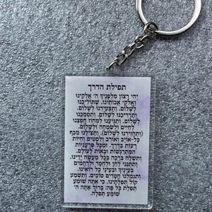 Pode incluir: Um cart&atilde;o branco com um chaveiro prateado anexado. O cart&atilde;o tem uma ora&ccedil;&atilde;o hebraica que diz "Tefilat HaDerech" (Ora&ccedil;&atilde;o para a jornada).