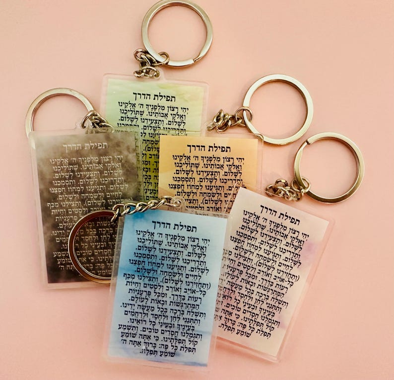 Pode incluir: Conjunto de quatro chaveiros com texto hebraico impresso em ret&acirc;ngulos de acr&iacute;lico transparente. Cada chaveiro tem um fundo de cor diferente com um efeito de aquarela. O texto nos chaveiros &eacute; uma ora&ccedil;&atilde;o para uma viagem segura.