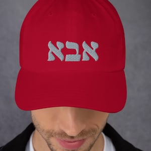 May include: A red baseball cap with the Hebrew word "אבא" embroidered in gray on the front.