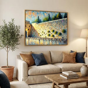 Puede incluir: Pintura al &oacute;leo enmarcada que representa un muro de piedra, un edificio y &aacute;rboles reflejados en el agua. La obra cuelga sobre un sof&aacute; beige con cojines marrones y azules. A la izquierda, un olivo en maceta.