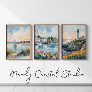 Puede incluir: Tres impresiones enmarcadas en acuarela que representan escenas costeras. Una muestra un velero, otra un puerto con barcos y flores, y la tercera un faro al atardecer. El texto "Moody Coastal Studio" está debajo.