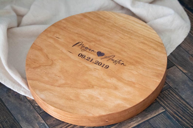 May include: A round wooden serving tray with a natural wood finish. The tray is engraved with the names "Megan & Austin" and the date "09.21.2019".