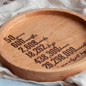 May include: A round wooden tray with the inscription "50 years, 600 months, 2,608 weeks, 18,262 days, 438,300 hours, 26,298,000 minutes, we've only just begun".