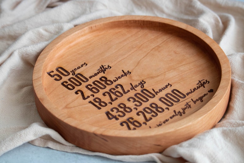 May include: A round wooden tray with the inscription "50 years, 600 months, 2,608 weeks, 18,262 days, 438,300 hours, 26,298,000 minutes, we've only just begun".