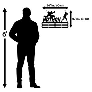 May include: Black metal sports medal display, 60 cm wide and 40 cm tall, with the name "NATHAN" and silhouettes of a hockey player and a baseball player. Features horizontal bars for displaying medals.