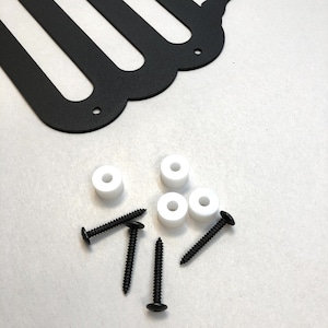 May include: Black metal wall art with a scalloped edge, white spacers, and black screws. The wall art features a distinctive design with several curved cutouts. Hardware is included for easy installation.