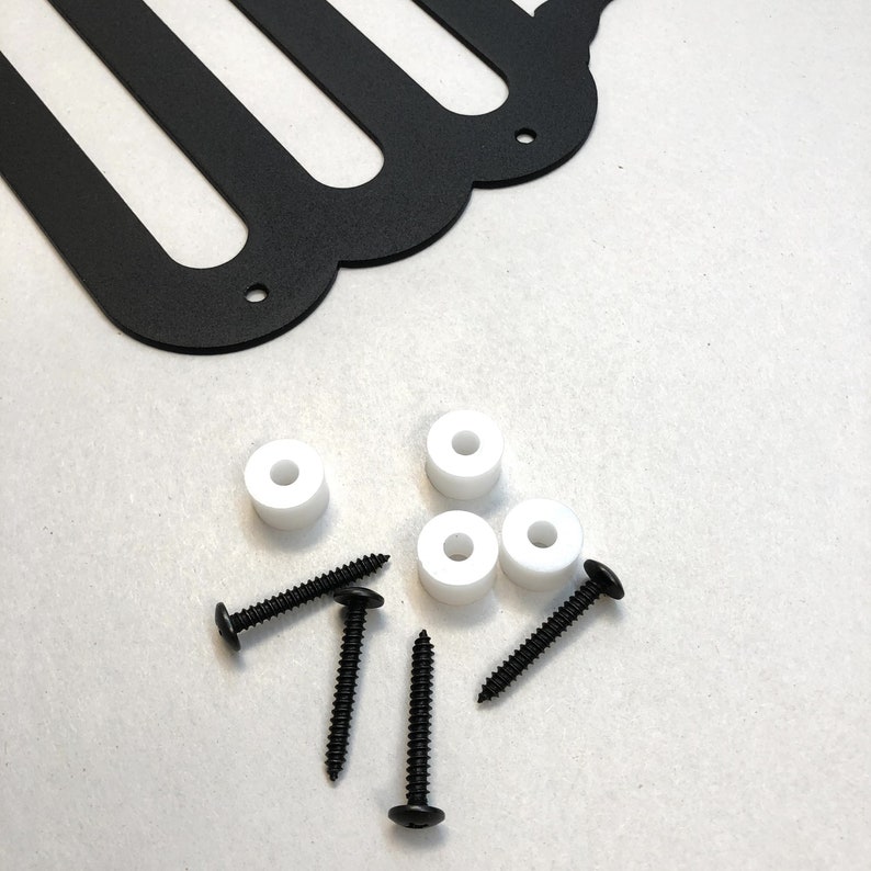 May include: Black metal wall art with a scalloped edge, white spacers, and black screws. The wall art features a distinctive design with several curved cutouts. Hardware is included for easy installation.