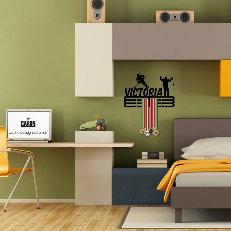 May include: Black metal medal display featuring the word "VICTORIAN" and silhouettes of a hockey player and a skier. It includes three bars for hanging medals and colourful ribbons.