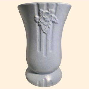 May include: A light blue ceramic vase with a floral design. The vase has a textured surface and a flared base.